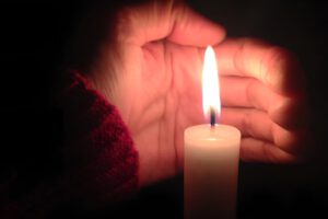 eine Hand, die schützend eine brennende Kerze hält