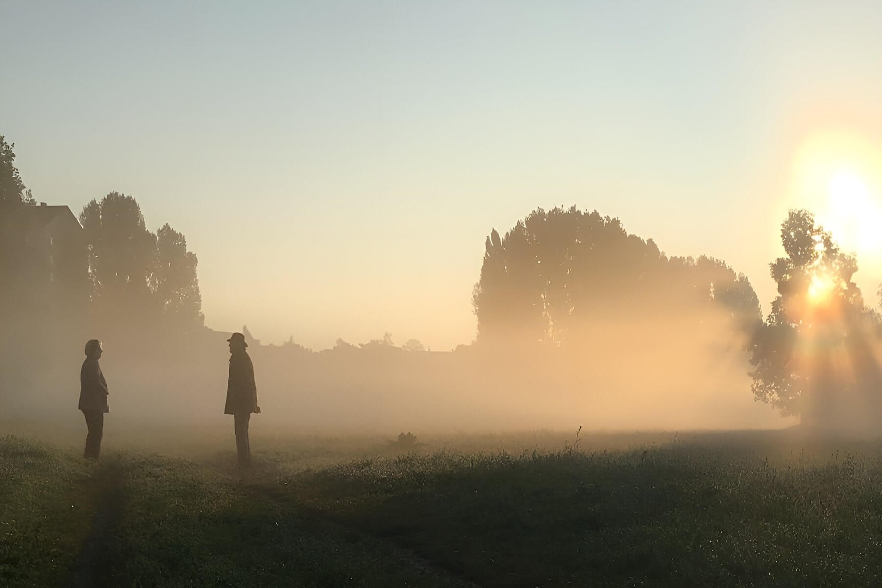 zwei Personen, die sich im Morgennebel gegenüberstehen, und sich über den Weg hinweg unterhalten